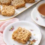 Pinterest graphic of a plate with a square piece of flapjack with a platter with more in the background.