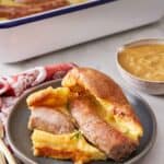 Pinterest graphic of a plate with a serving of toad in the hole with a baking dish in the back along with a bowl of the gravy.