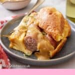Pinterest graphic of a plate of toad in the hole with a fork with some gravy drizzled over on top.