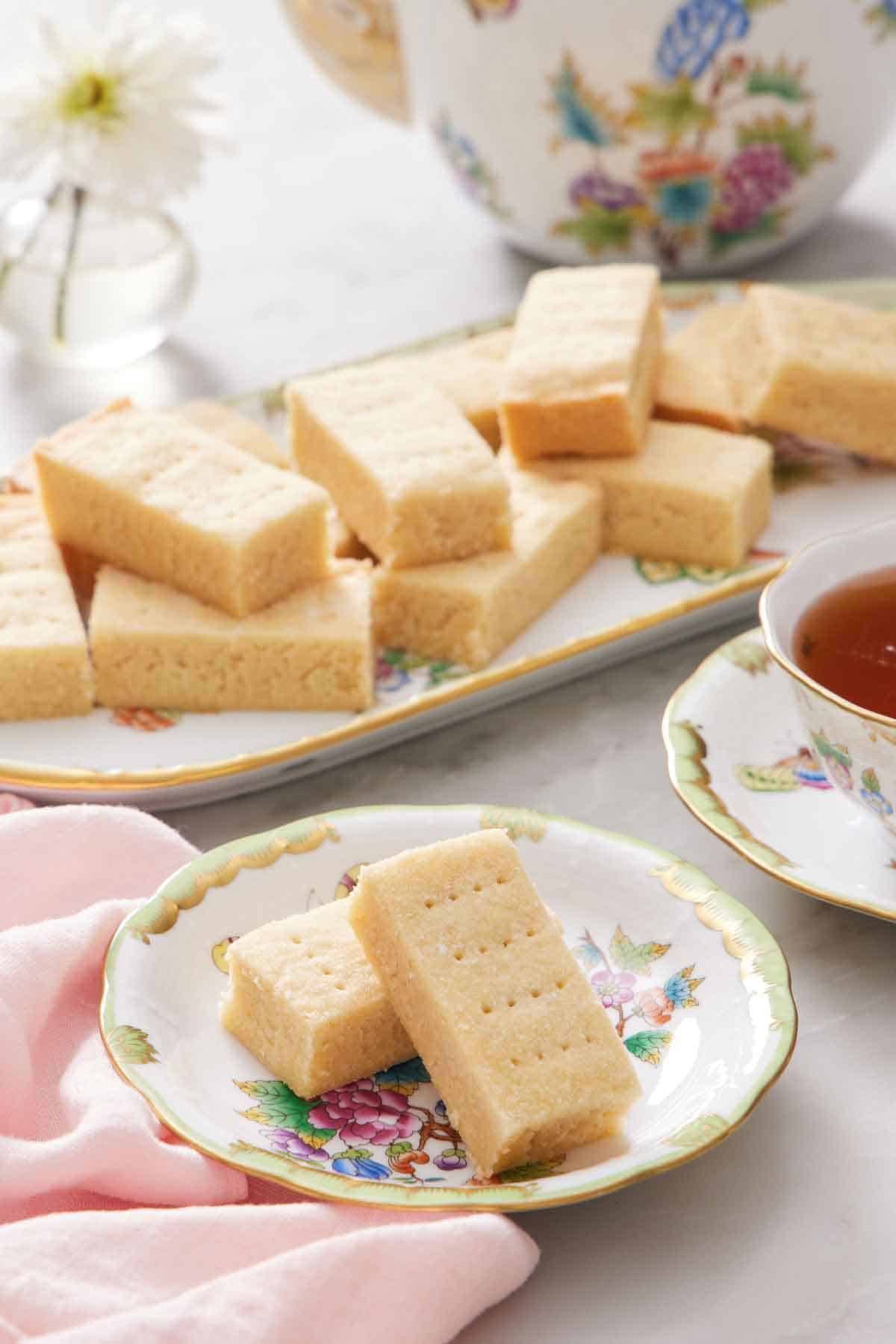 A plate with two rectangular pieces of shortbread biscuits with more on a platter in the background.